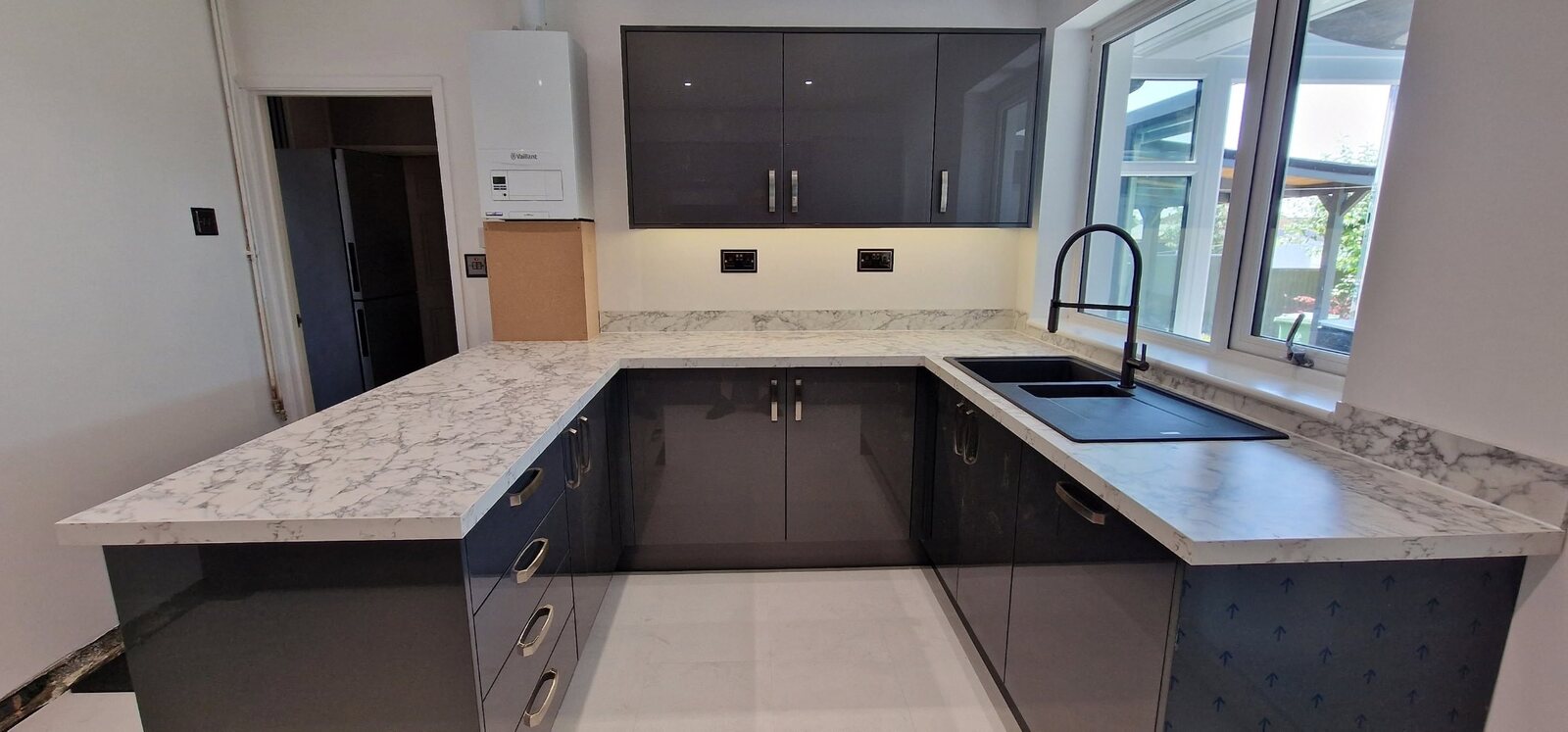 Completed grey gloss kitchen with marble-effect peninsula and black sink